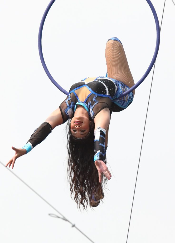 A Cyber Cirque performer hangs in the air on a ring with no safety attachments.