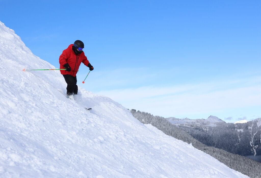 A skier turns down Pan Dome beneath blue skies.