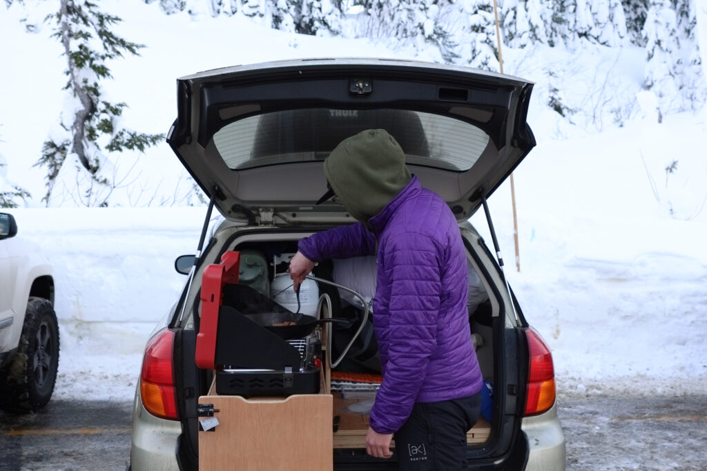 Conner Pape, 25, cooks sausages from the back of his Subaru, which he plans to sleep in to maximize two days on the mountain.