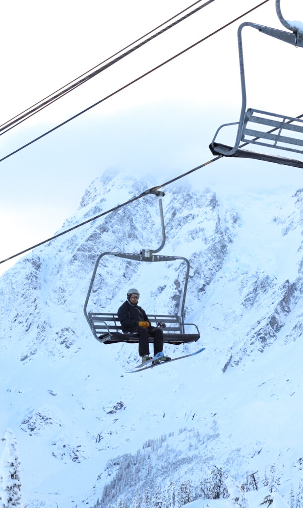 A skier rides Chair 6 with Shuksan looming in the background.