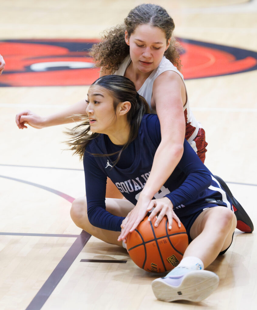 Squalicum’s Lexi Robbins grabs a loose ball as Bellingham’s Malia Hanks reaches over her.