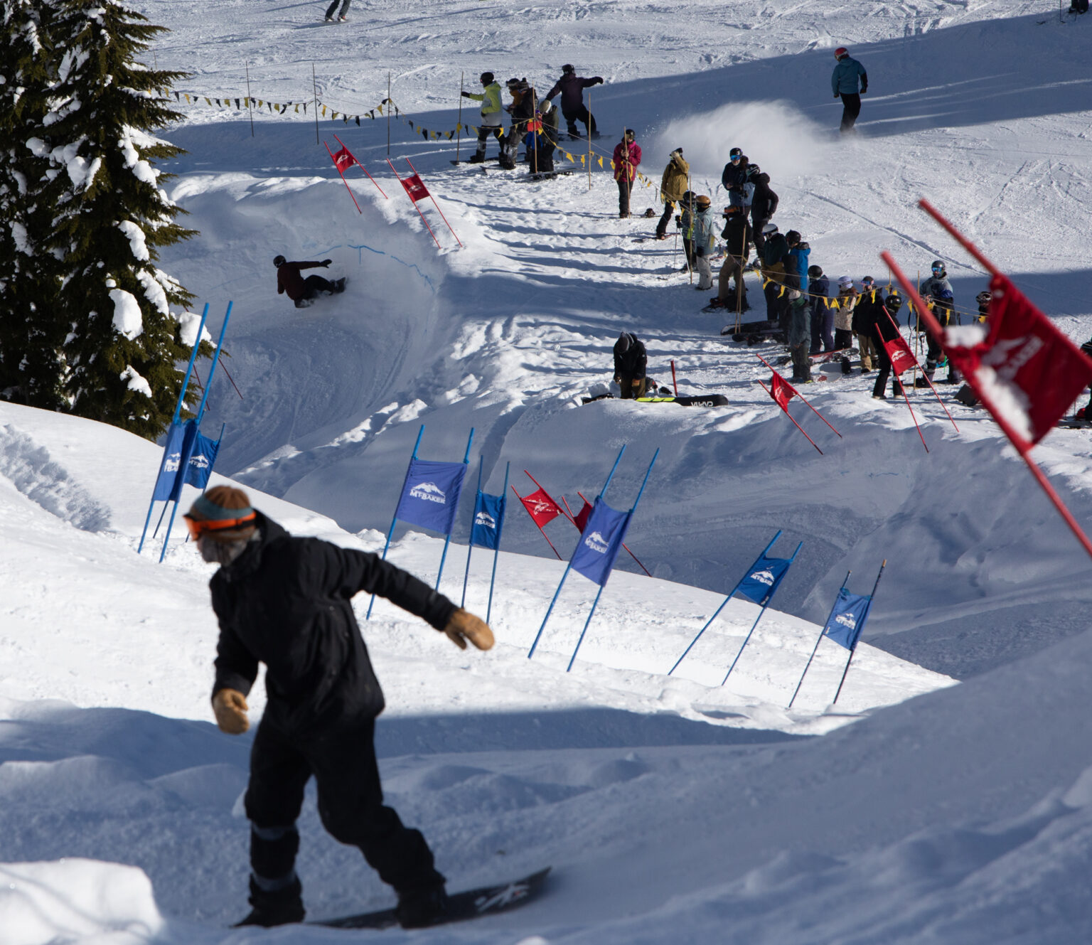 Two snowboarders make their way down the course as onlookers watch them take steep turns.