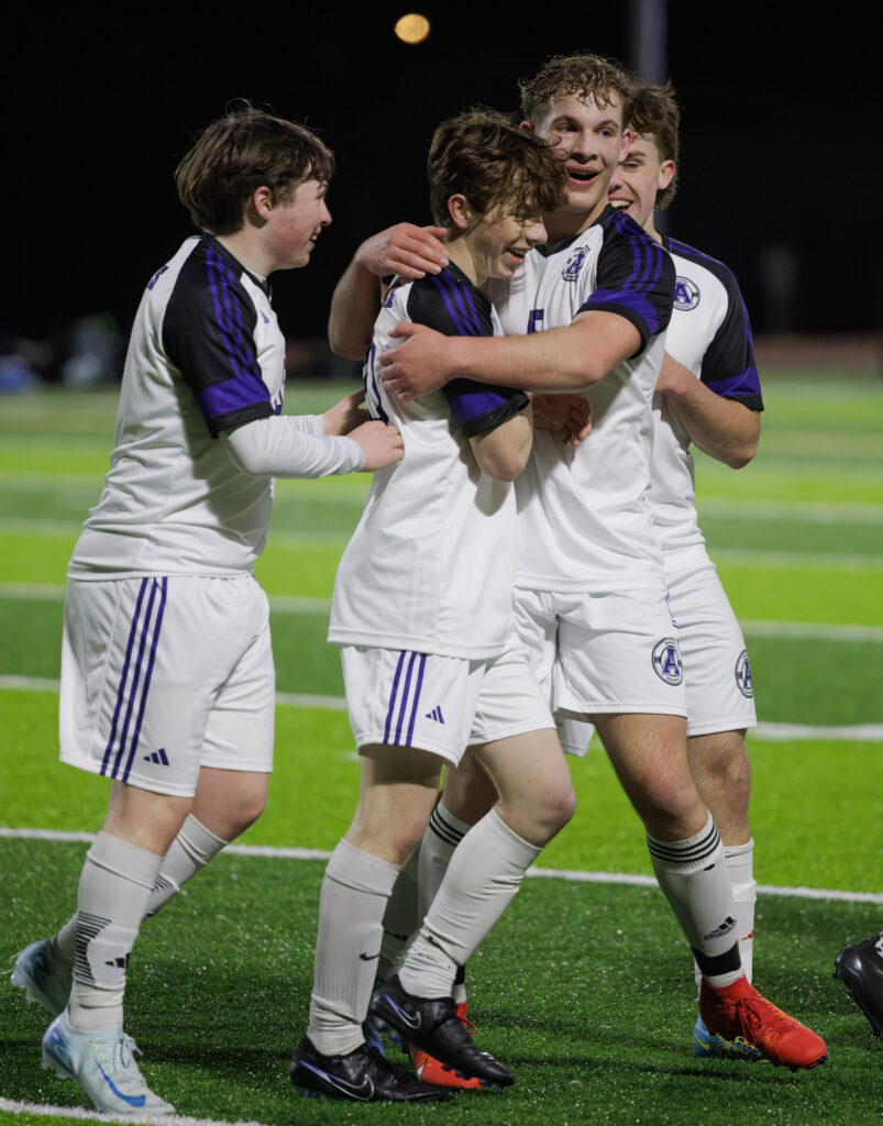 Anacortes teammates surround Owen Foley after he scores a goal on a free kick.